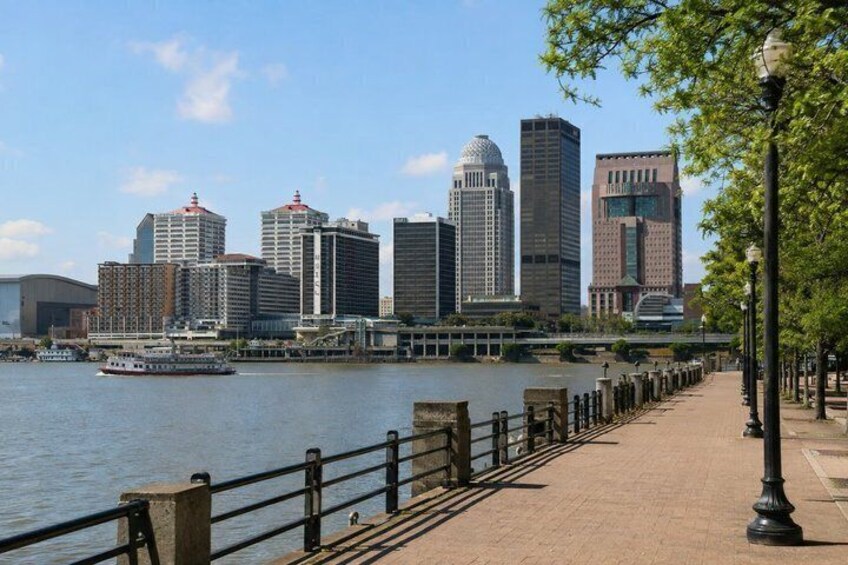 A river with a boat, a city skyline, and a pedestrian walkway. 3