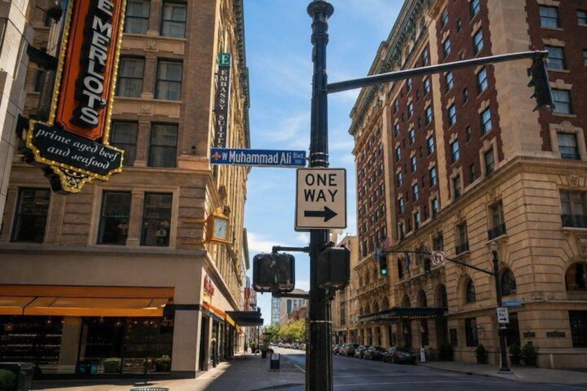 A street corner with a 'One Way' sign, a street sign for 'Muhammad Ali St,' and a building with a sign for 'Emperors.' 4