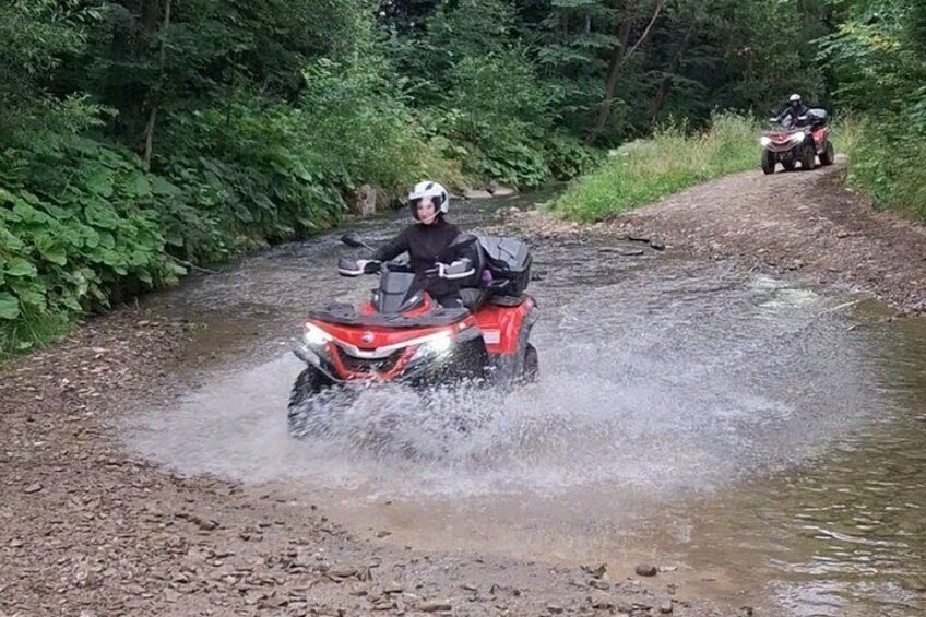 A person riding a red ATV through a shallow stream. 2