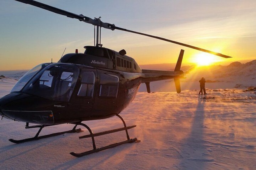A helicopter on a snowy surface with a person standing in the background. 1