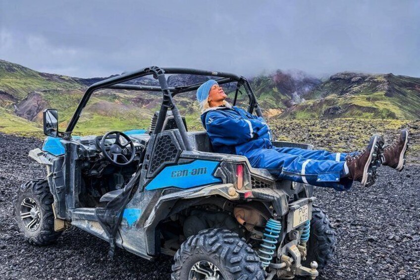 A person in blue gear sitting in a blue and black off-road vehicle with a rugged landscape in the background. 4