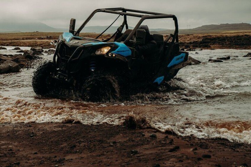 A blue and black off-road vehicle driving through a shallow water crossing on a rocky terrain. 3