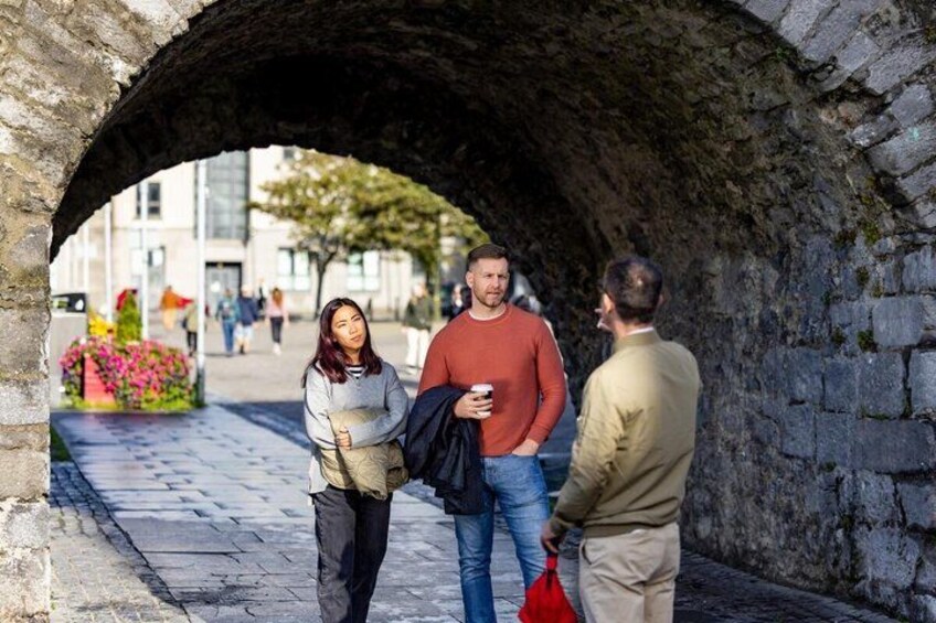 Un arco de piedra, una persona sosteniendo una bolsa roja y otra persona con una taza de café. 3