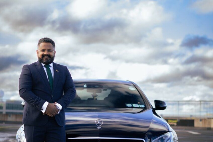 Un hombre con traje de negocios parado junto a un coche negro con el logotipo de Mercedes. 2