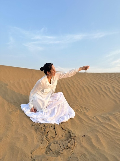 A person sitting on a sand dune with a clear sky in the background. 4