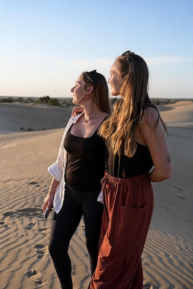 Two people standing on a sandy beach with dunes in the background. 1