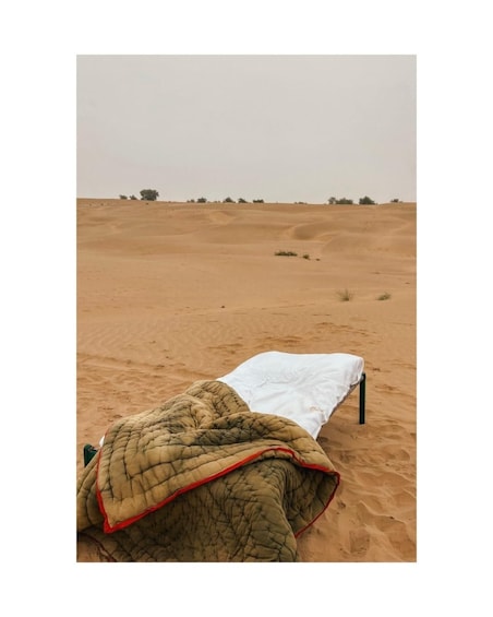 A bed in a desert with a blanket and a white sheet. 3