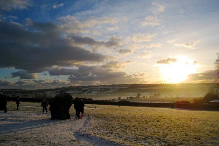 A sunset over a snowy landscape with people walking and a large rock formation in the foreground. 4