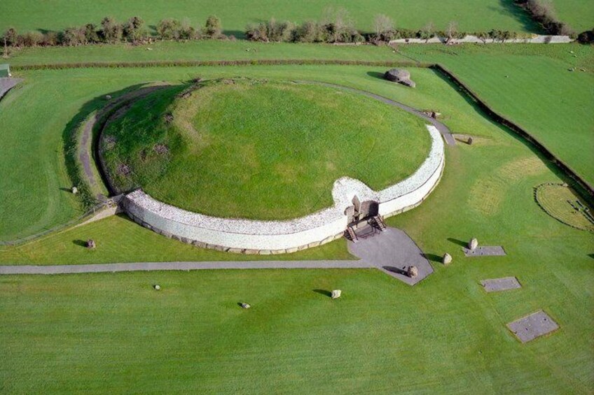 An aerial view of a circular stone structure with a central stone building, surrounded by a stone wall and grassy fields. 1