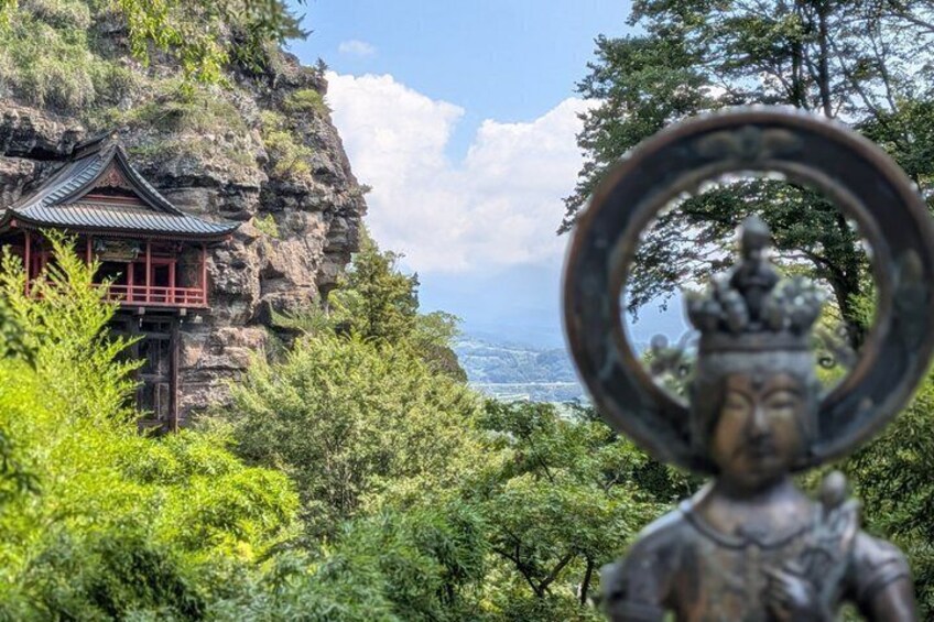 A traditional building on a cliff, lush greenery, and a statue with a halo. 3