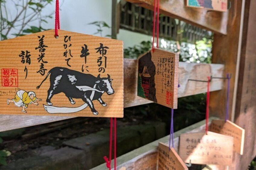 A wooden sign with Japanese characters and a black and white cow illustration. 4