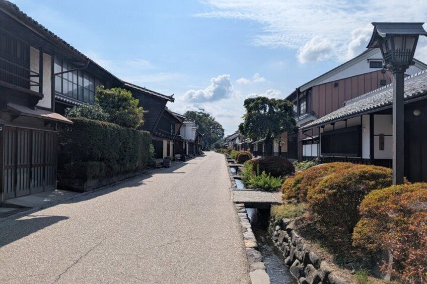 A traditional Japanese street with wooden houses, a stone path, and a small stream. 2