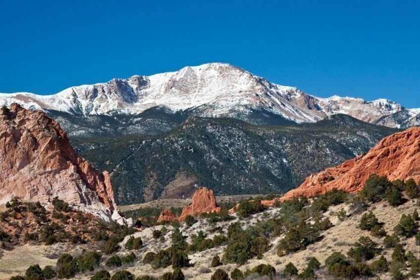 A mountain range with snow-capped peaks, red rock formations, and sparse vegetation. 2