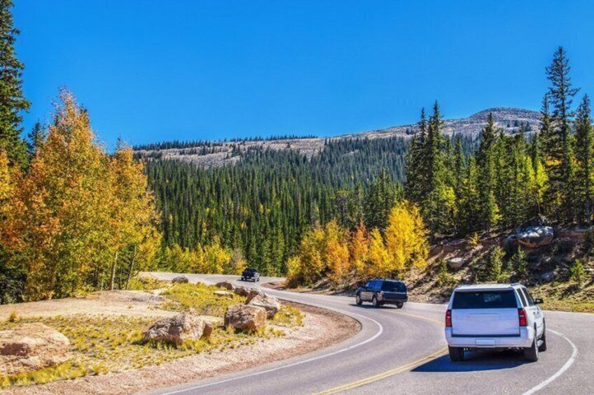 A winding mountain road with vehicles, autumn foliage, and a forested backdrop. 4