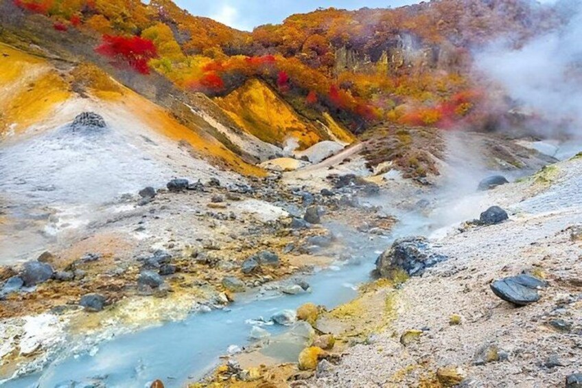 A geothermal area with a river, steam vents, and autumn-colored trees. 5