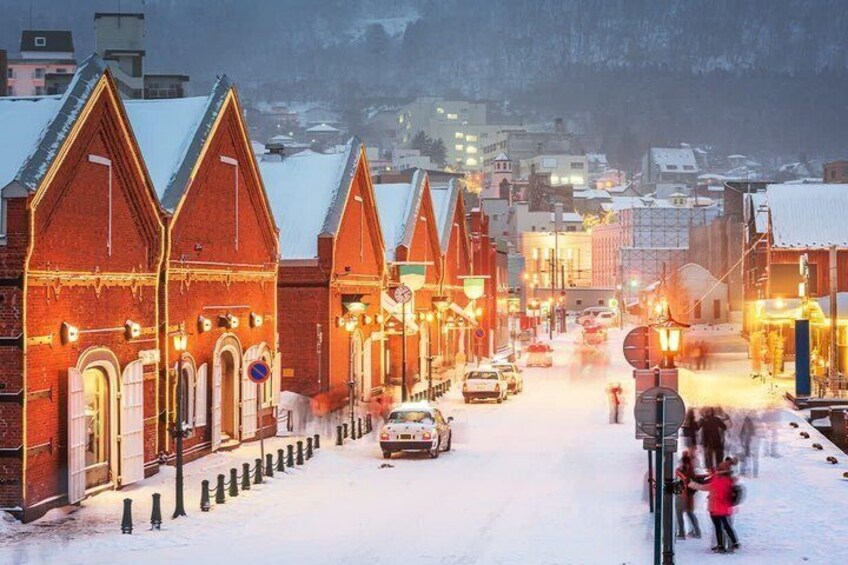 A snow-covered street lined with red brick buildings, some with lights on. 2