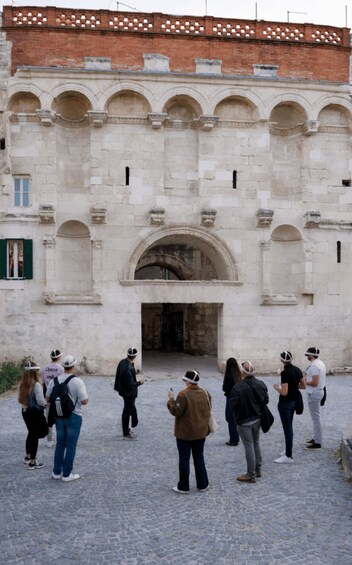 A group of people standing in front of a historic stone building with arches and a large entrance. 3
