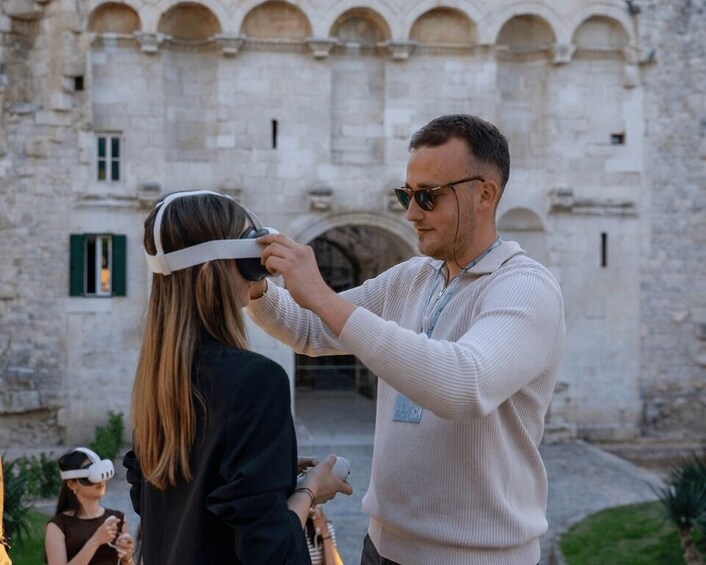 A person assisting another with a virtual reality headset in front of a historic building. 2