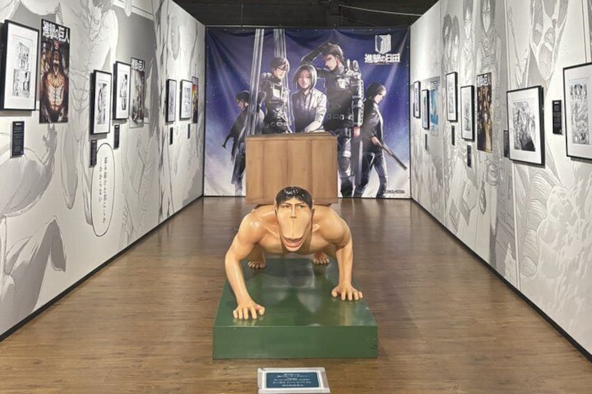 A museum exhibit with a mannequin in a push-up position on a green platform, surrounded by framed artwork on the walls. 3
