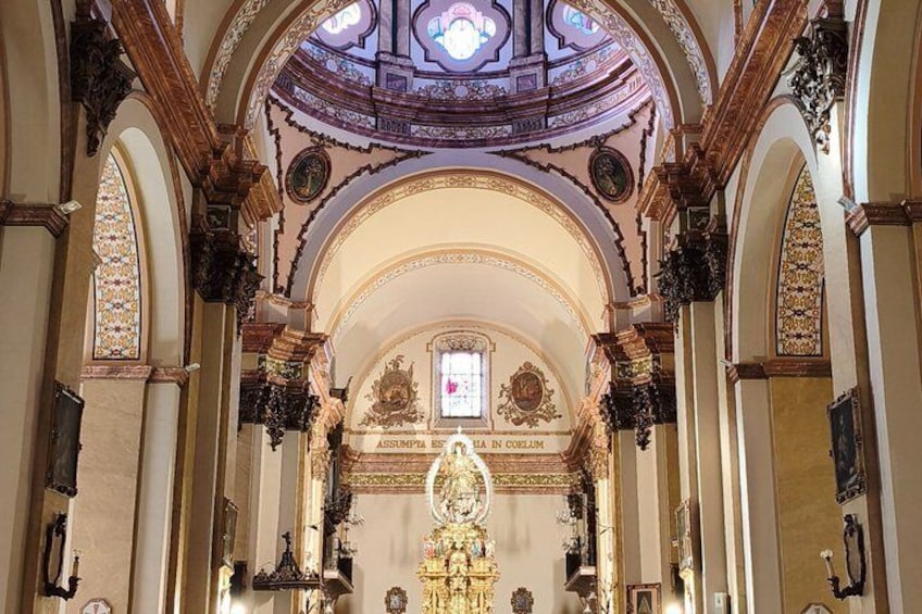 An ornate church interior with a central altar, stained glass windows, and intricate architectural details. 5
