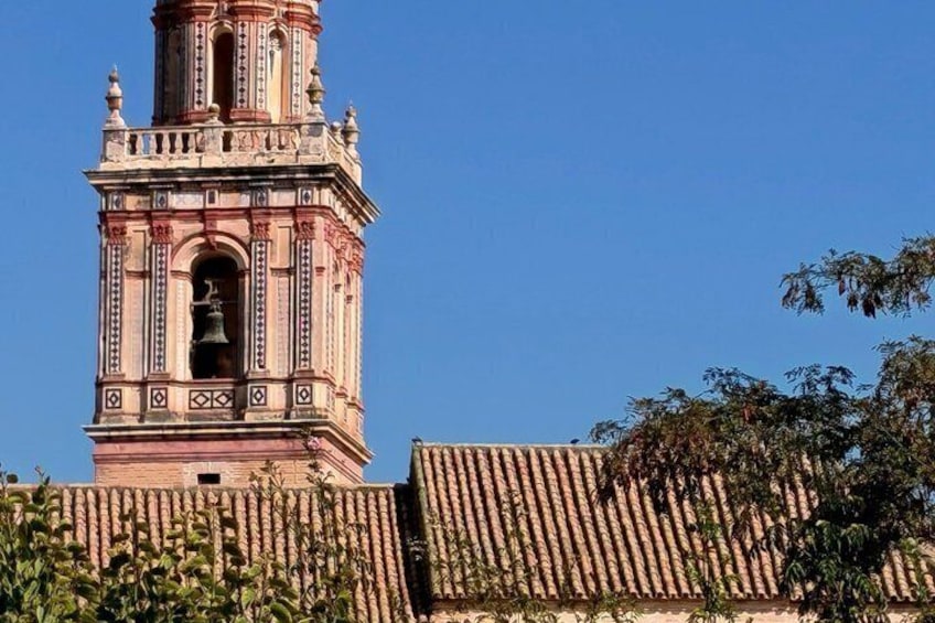 A tall, ornate tower with a bell, surrounded by greenery and a clear blue sky. 2
