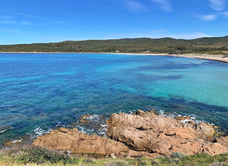 A coastal landscape with clear blue waters, rocky shoreline, and distant hills. 3