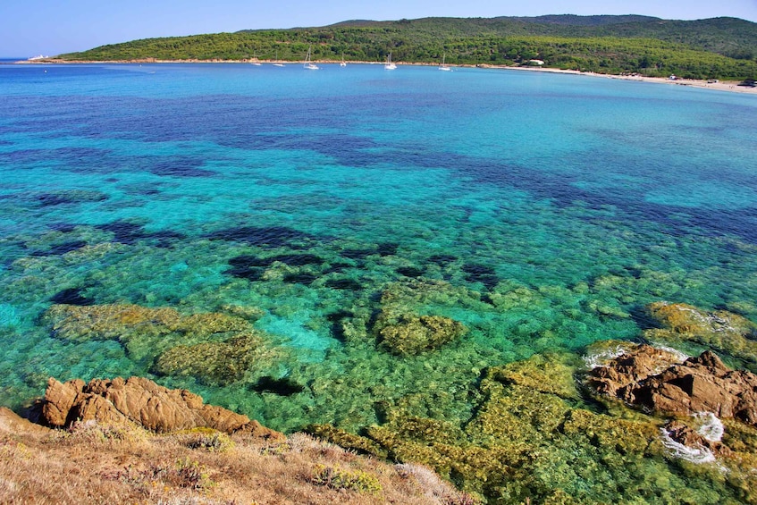 A coastal landscape with clear turquoise waters, rocky outcrops, and a distant hill with vegetation. 2