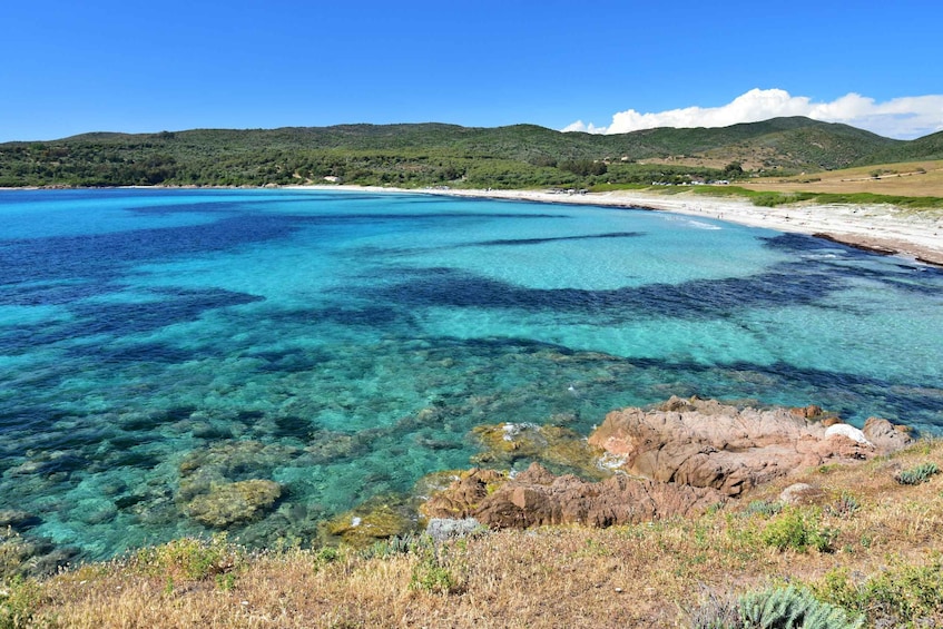 A coastal landscape with clear turquoise waters, rocky outcrops, and a sandy beach. 4