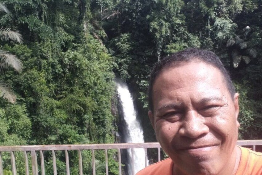 A person standing in front of a waterfall with dense greenery in the background. 2