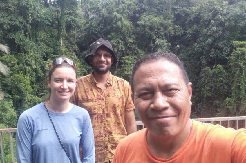 Three people standing outdoors with dense green foliage in the background. 3