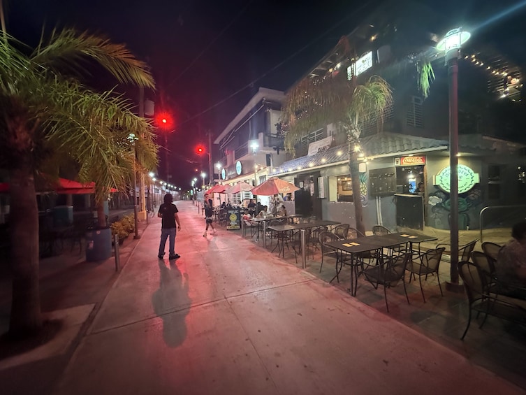 A nighttime street with outdoor seating, palm trees, and illuminated buildings. 4