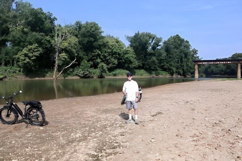 A person standing by a river with a bicycle and a bridge in the background. 4