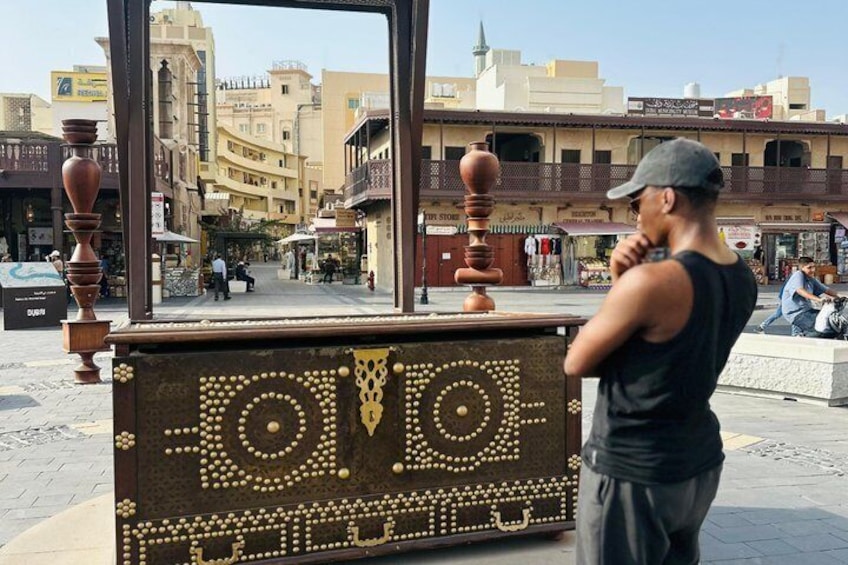 A man standing in front of a decorative kiosk with intricate designs, in a busy urban street with buildings and shops. 3