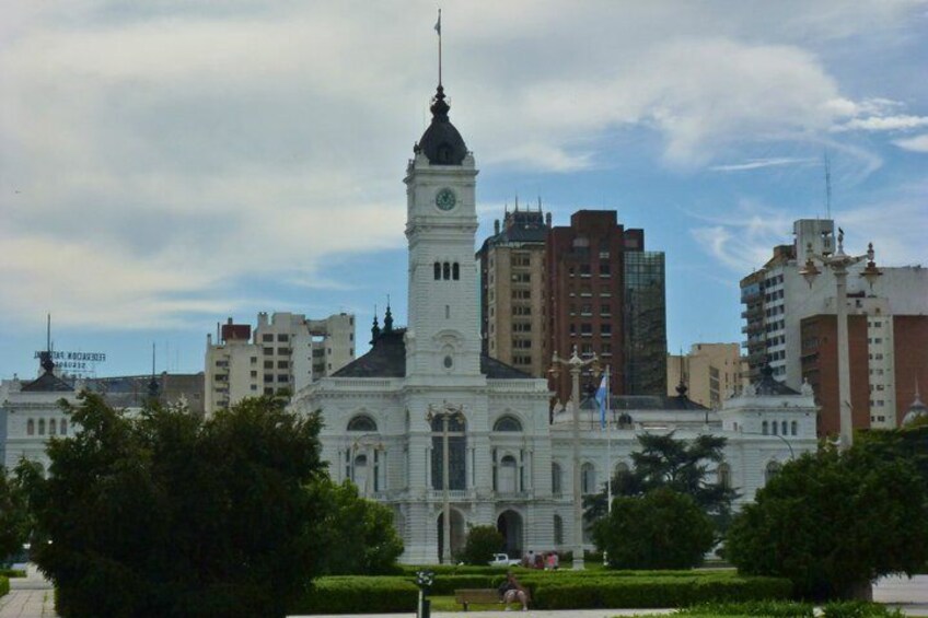 A historic building with a clock tower, surrounded by modern high-rise buildings and greenery. 5