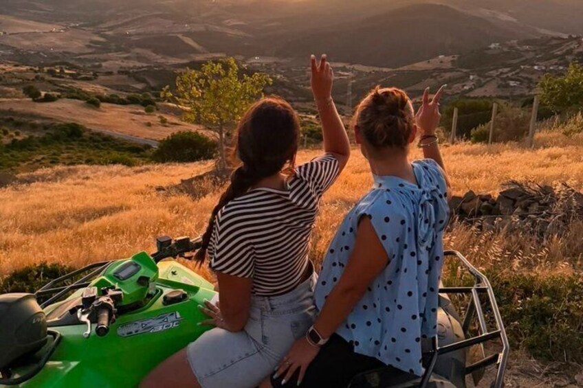Two people sitting on a green ATV, overlooking a hilly landscape during sunset. 5