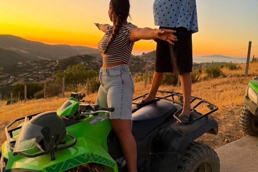 A person standing on a green ATV with a sunset in the background. 4