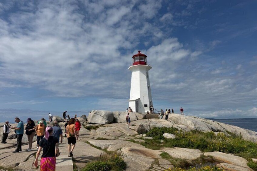 A lighthouse on a rocky outcrop with people walking around. 4