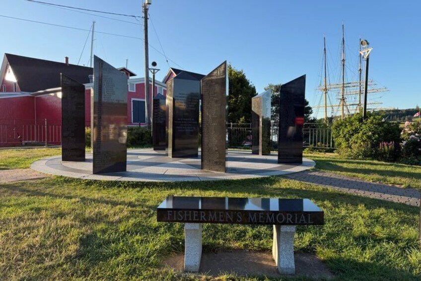 A Fishermen's Memorial with a plaque, a red building, and a ship in the background. 5