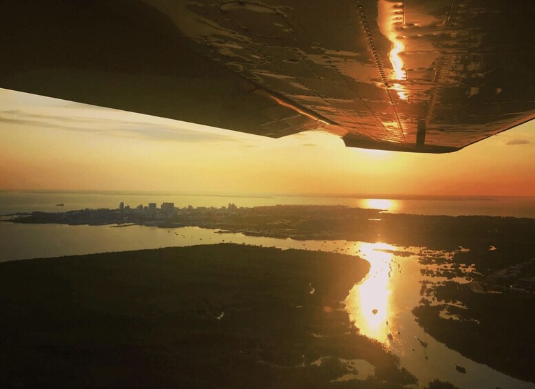 An airplane wing casting a shadow over a sunset landscape with a city skyline in the distance. 3