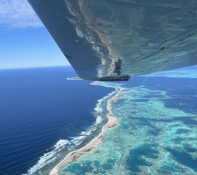 An aerial view of a coastal area with clear blue waters, a sandy beach, and a coral reef system. 1