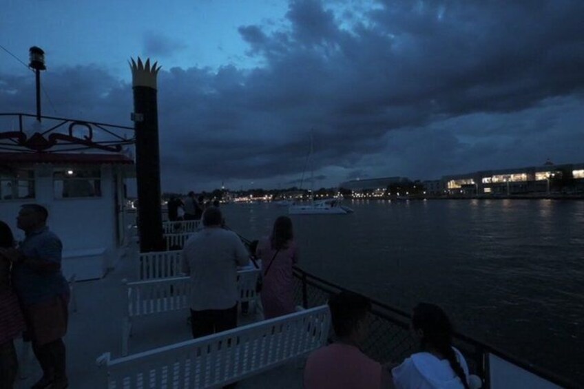 A waterfront scene with people standing on a dock, a boat, and buildings in the background. 4