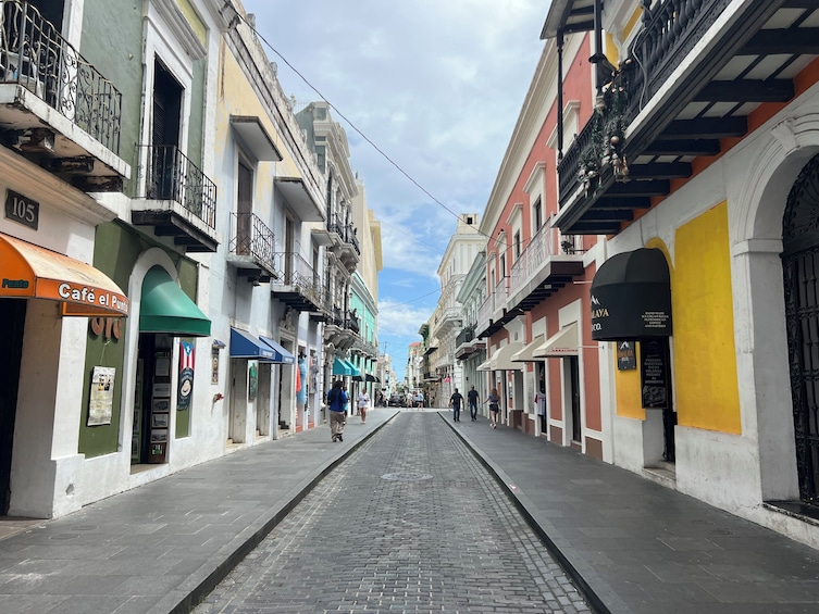 A cobblestone street lined with colorful buildings, a café, and various shops. 4