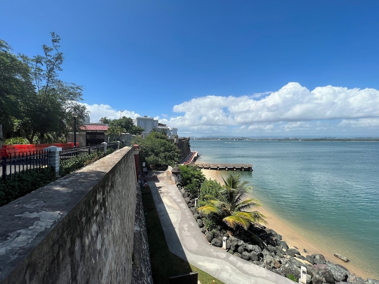 A coastal promenade with a stone wall, a beach, and a clear blue sky. 3