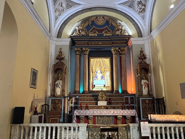 An ornate church interior with a central altar, statues, and a large stained glass window. 5