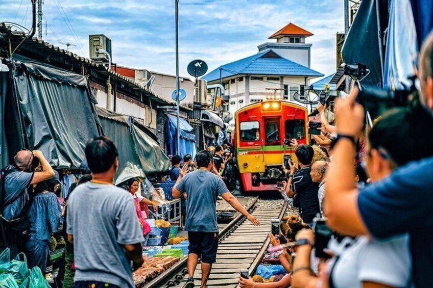 A crowded market with people and a train passing through. 1