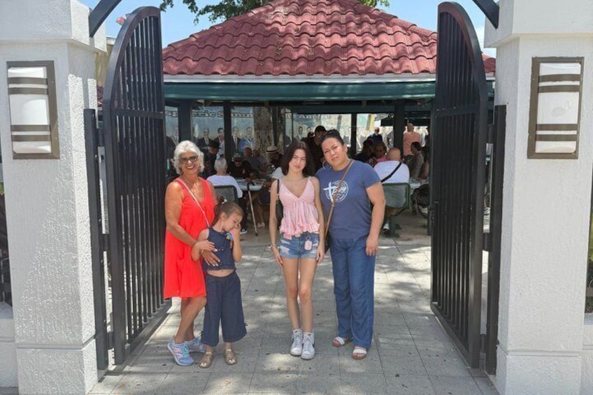 A family of four standing in front of a gated entrance with a red-tiled roof in the background. 2