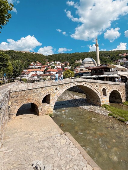 A stone bridge over a river, a mosque with a minaret, and a hillside town. 1