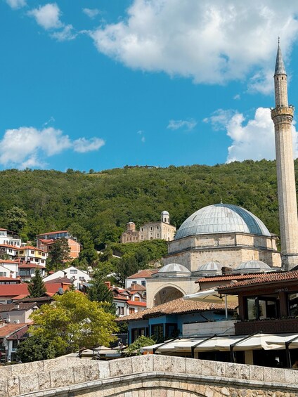 A mosque with a tall minaret and a dome, surrounded by a hillside town with buildings and trees. 5