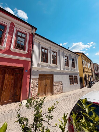 A cobblestone street lined with colorful buildings, a wooden door, and a parked car. 3
