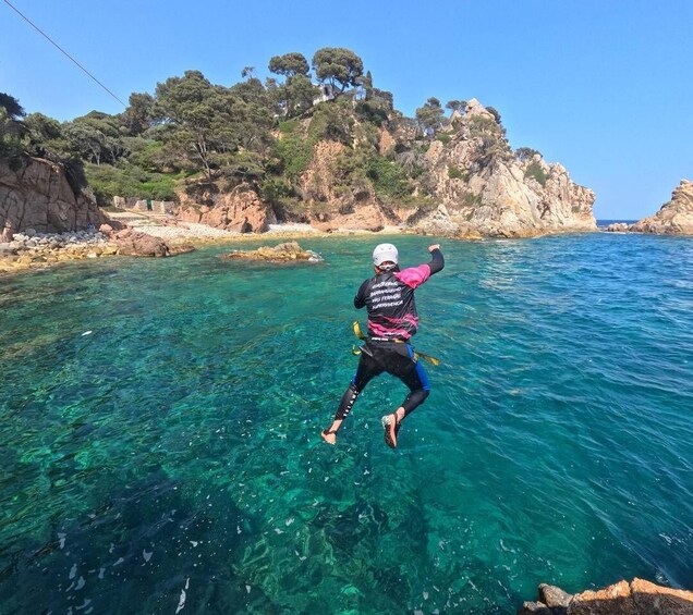 A person jumping into clear blue water with rocky cliffs and trees in the background. 1